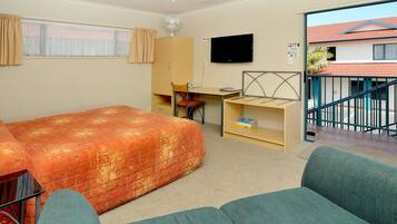 Een kamer met een bed, een bureau, een stoel, een televisie en uitzicht op een gebouw.