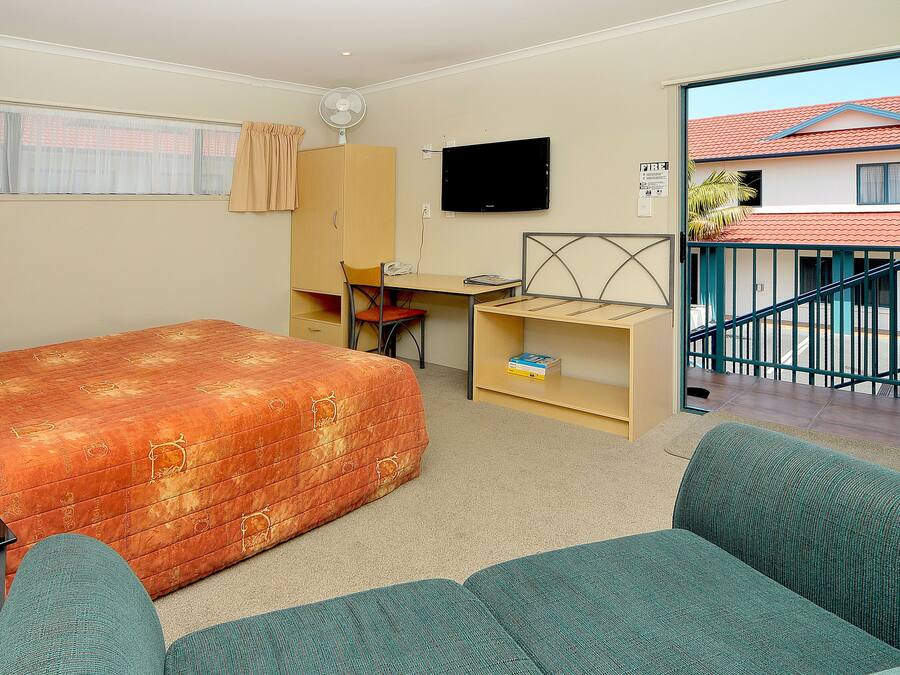 Een kamer met een bed, een bureau, een stoel, een televisie en uitzicht op een gebouw.