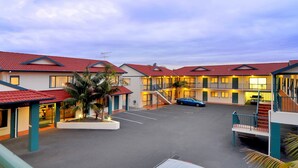 A motel with multiple units, a parking area, and a central courtyard with palm trees. - Academy at Botany Motor Inn (Auckland)