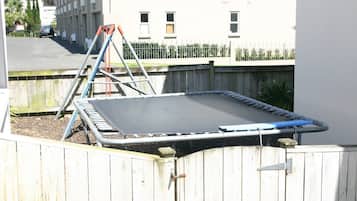 Een trampoline in een omheinde achtertuin met een houten schutting, een ladder en een metalen hek op de achtergrond.