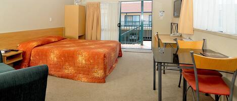 A hotel room with a bed, a desk, a chair, a wardrobe, and a balcony with a view.