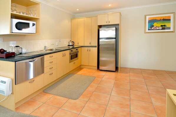 A modern kitchen with stainless steel appliances, wooden cabinets, and a tiled floor.