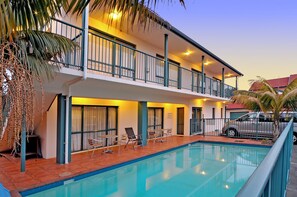 A hotel with a pool, outdoor seating, and a carport.