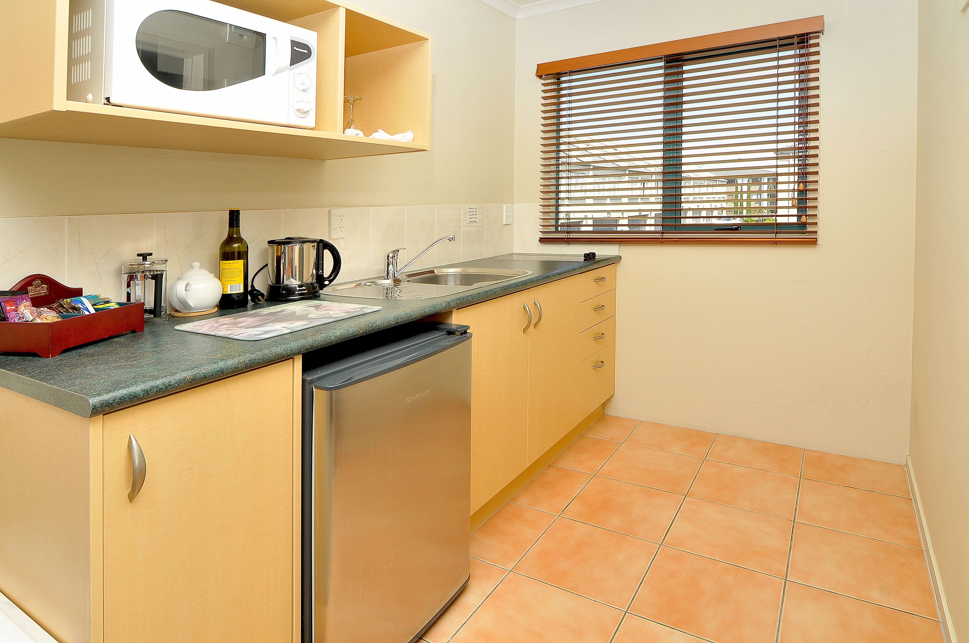 Una cocina compacta equipada con microondas, lavamanos y refrigerador pequeño.