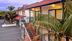 A hotel with a red-tiled roof, a staircase with blue railings, and a parking lot. - Academy at Botany Motor Inn (Auckland)