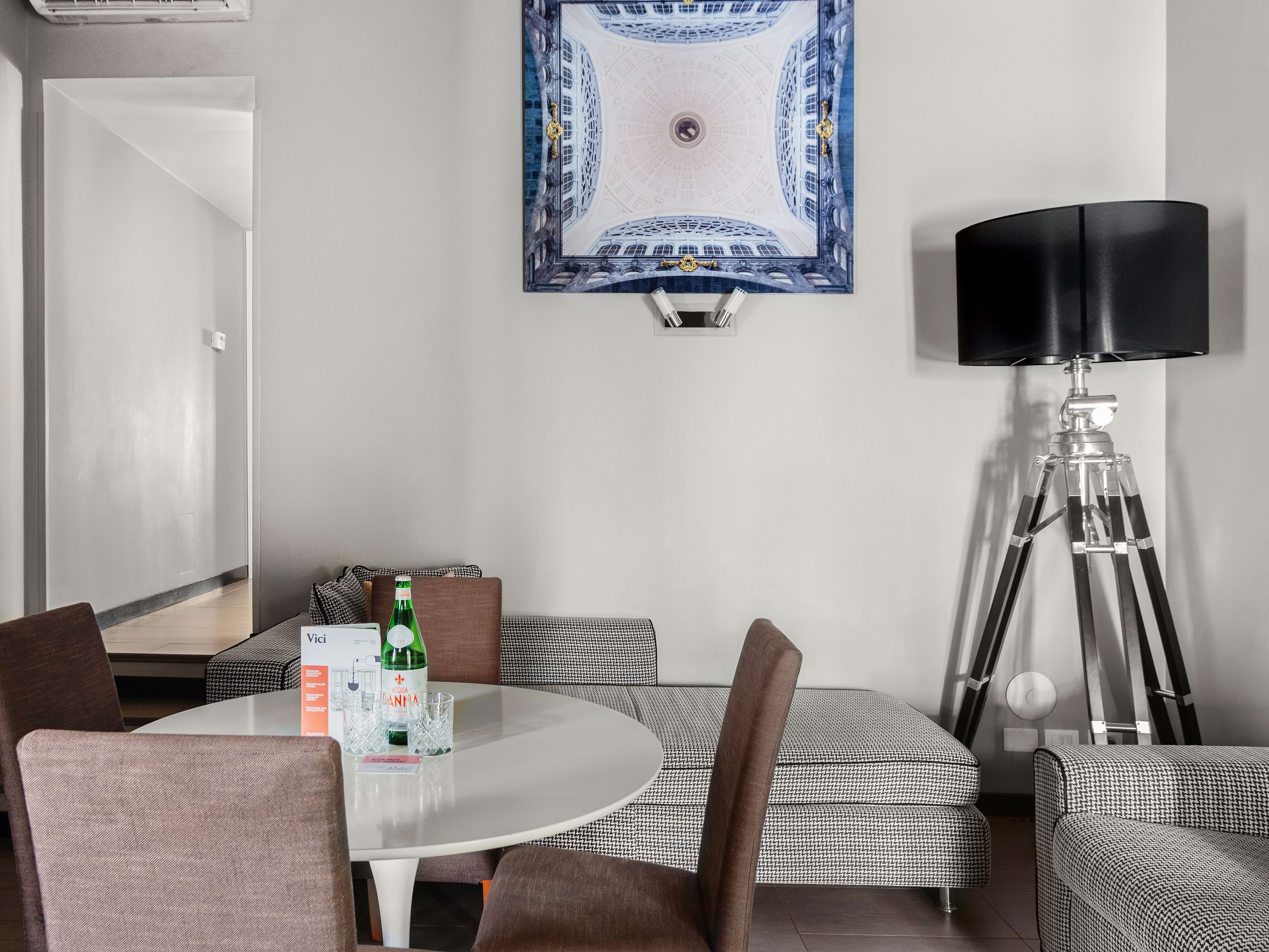 A hotel room with a round dining table, a sofa, a lamp, and a framed artwork on the wall.