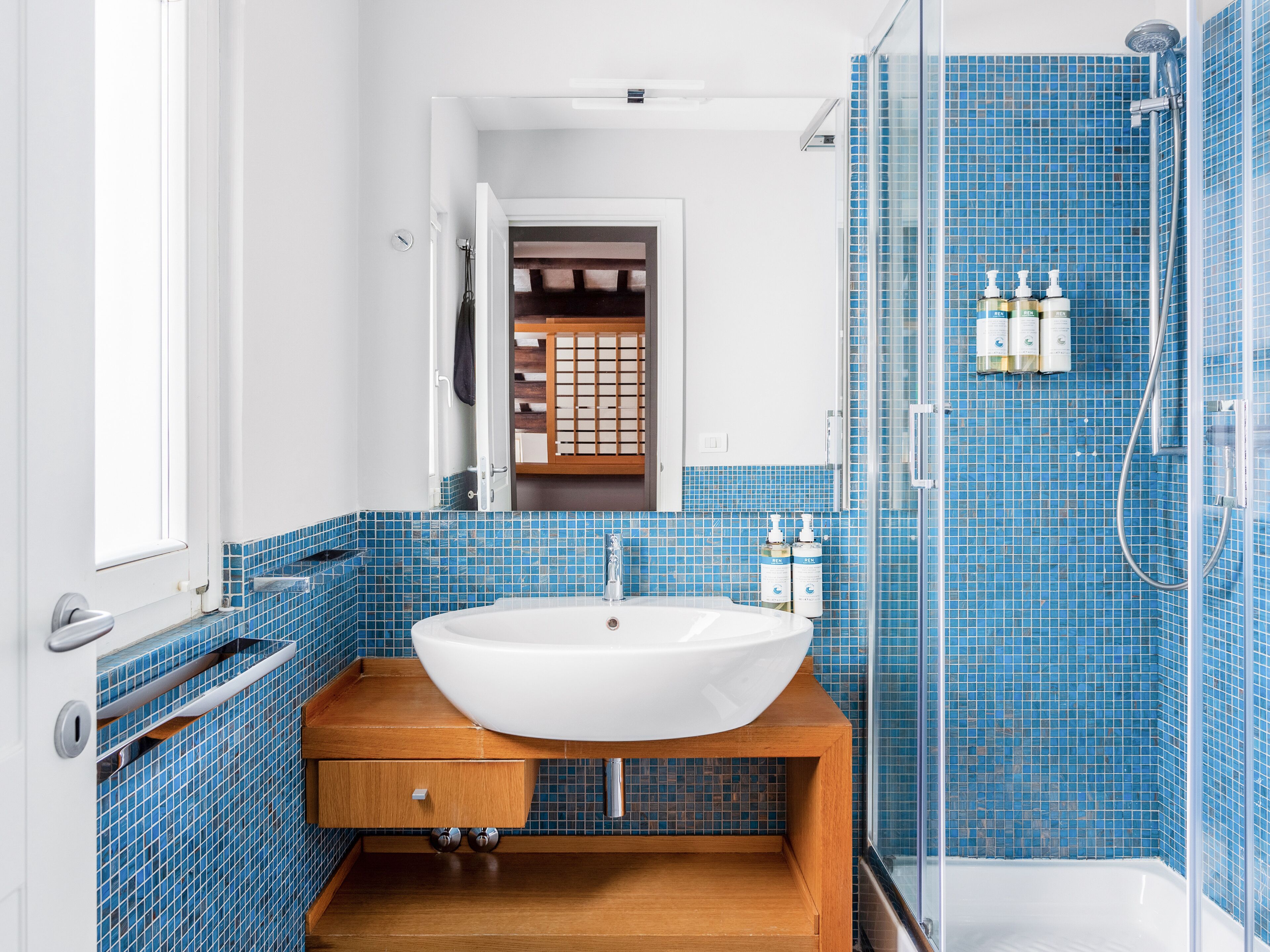 A bathroom with a white sink, blue tiled walls, and a glass shower enclosure.