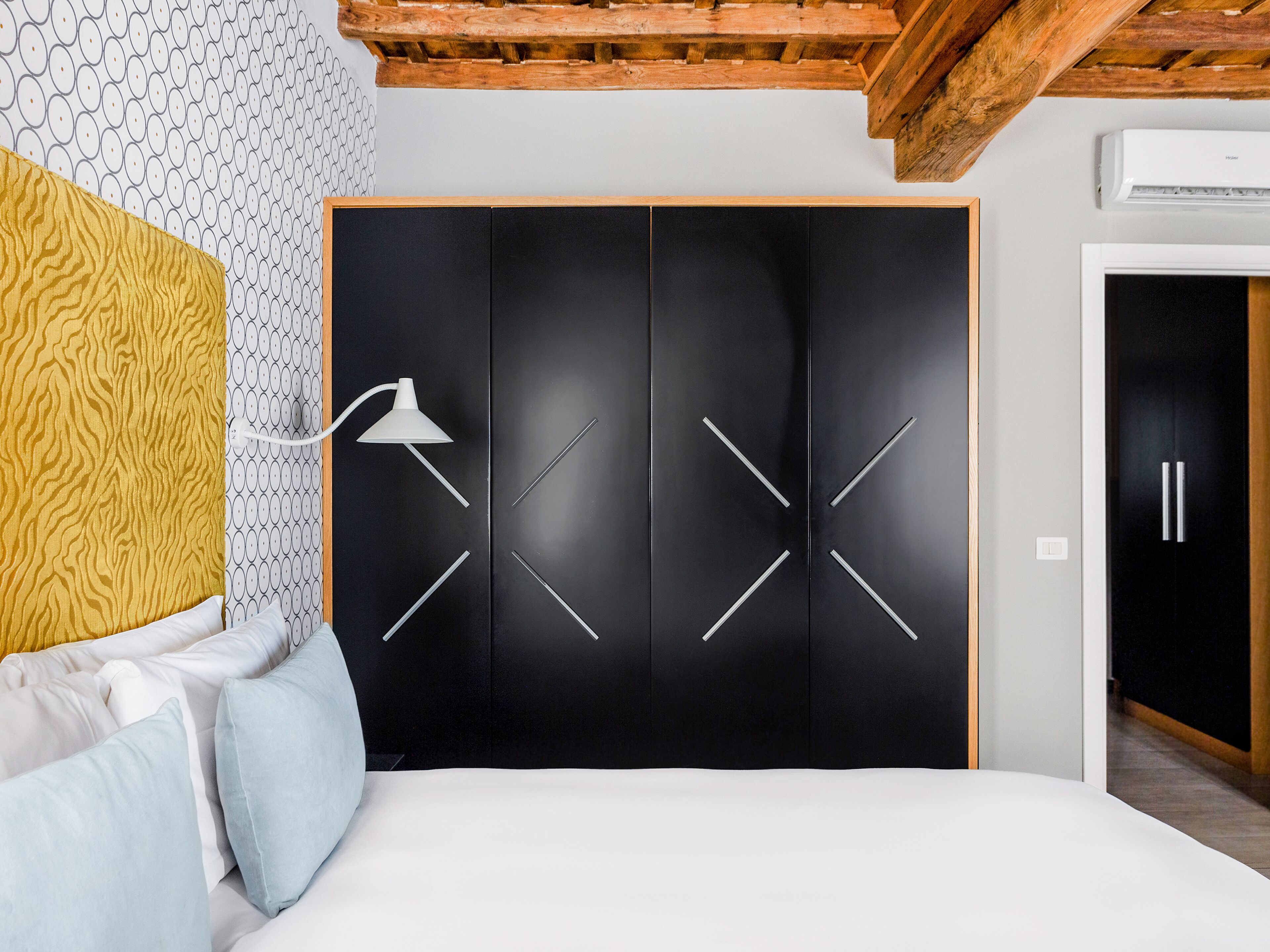 A bedroom with a black wardrobe, a white bed, and a patterned wall.