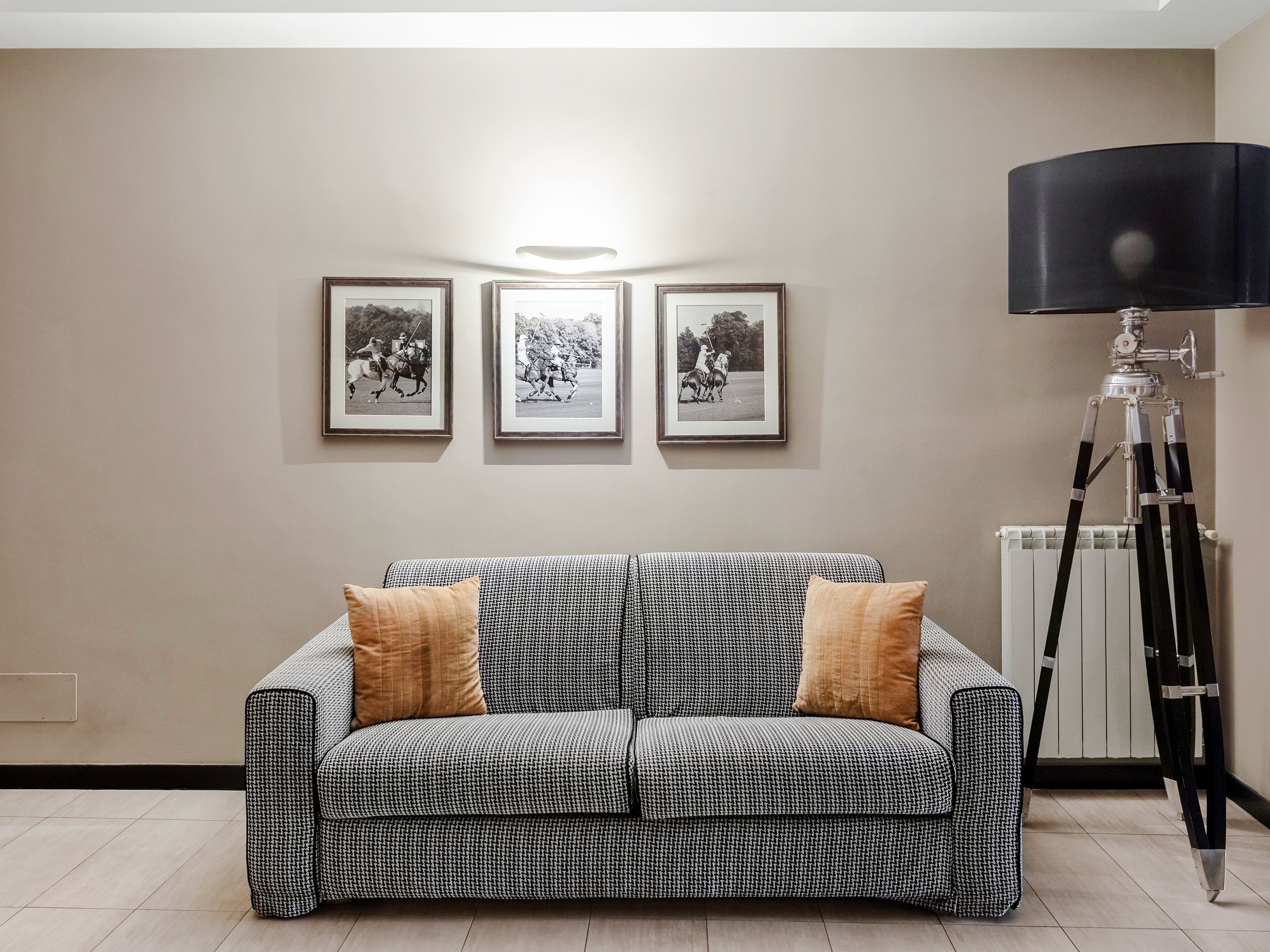 Een moderne woonkamer met een gestreept sofa, drie ingelijste foto’s aan de muur, en een statief met een camera op de vloer.
