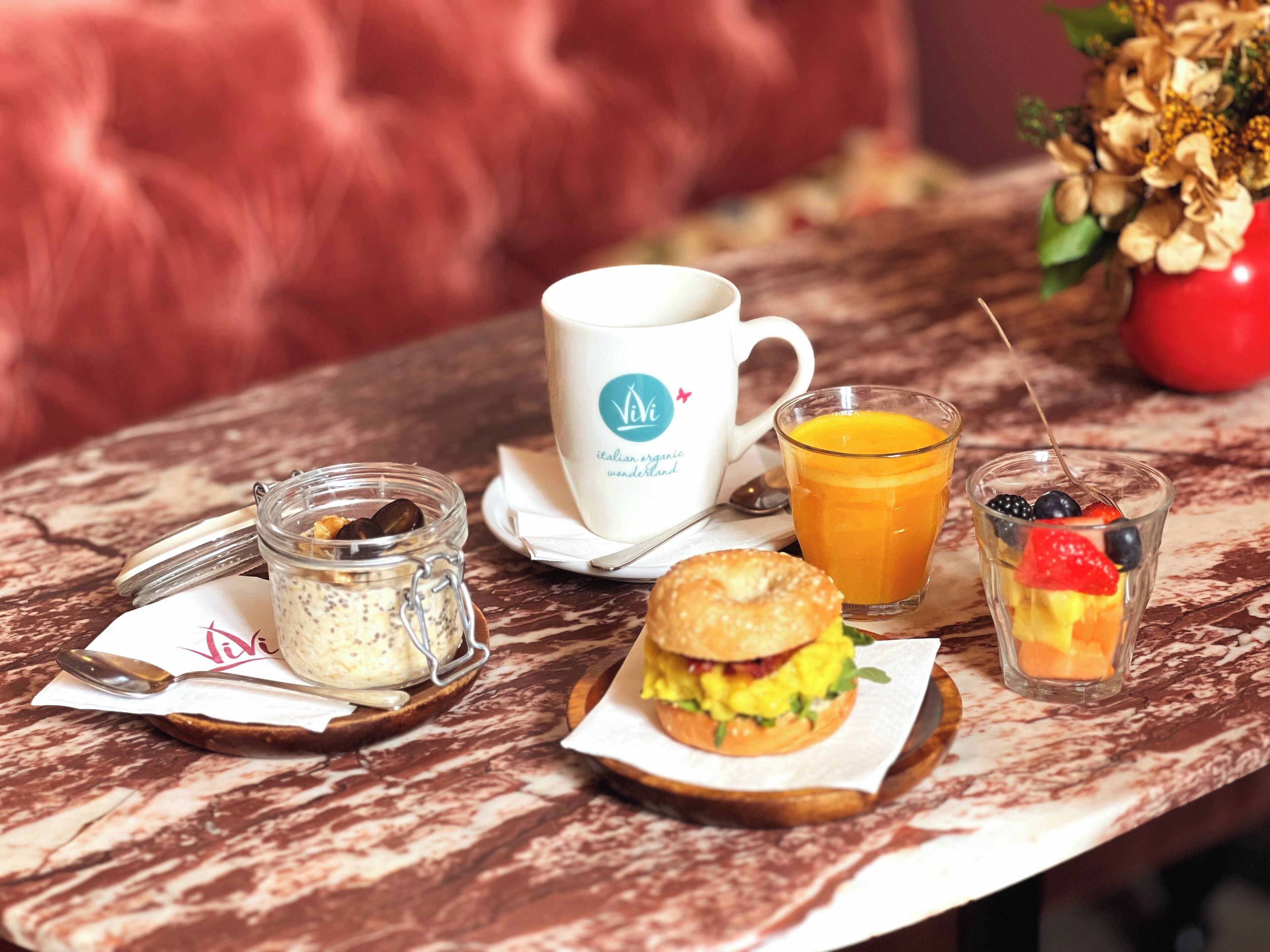 A breakfast setting with a cup, juice, sandwich, and a small jar on a marble table.
