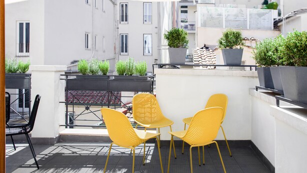 A balcony with yellow chairs and potted plants, overlooking a cityscape with buildings. - Numa Rome Vici (Rome)