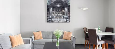 A modern living room with a black coffee table, a checkered sofa, and a dining area with a white table and brown chairs.