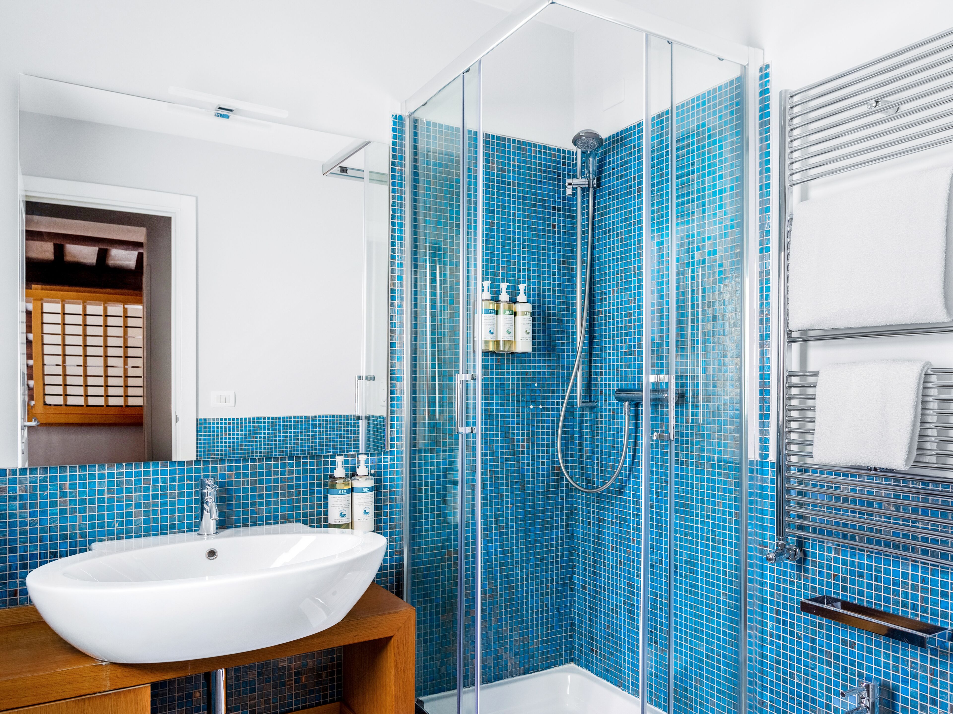 A bathroom with a white sink, blue mosaic tiles, a glass shower enclosure, and a towel rack.
