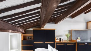 A modern bedroom with a lofted ceiling, a bed with white linens, a wooden nightstand, a built-in wardrobe, and a kitchenette area. - Numa Rome Vici (Rome)