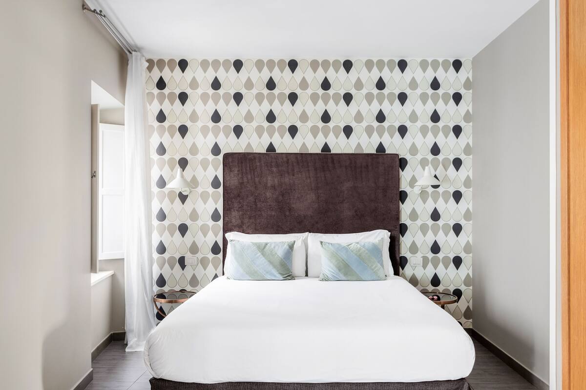 Une chambre à coucher bien aménagée, avec un grand lit, une tête de lit sombre et un papier peint à motifs.