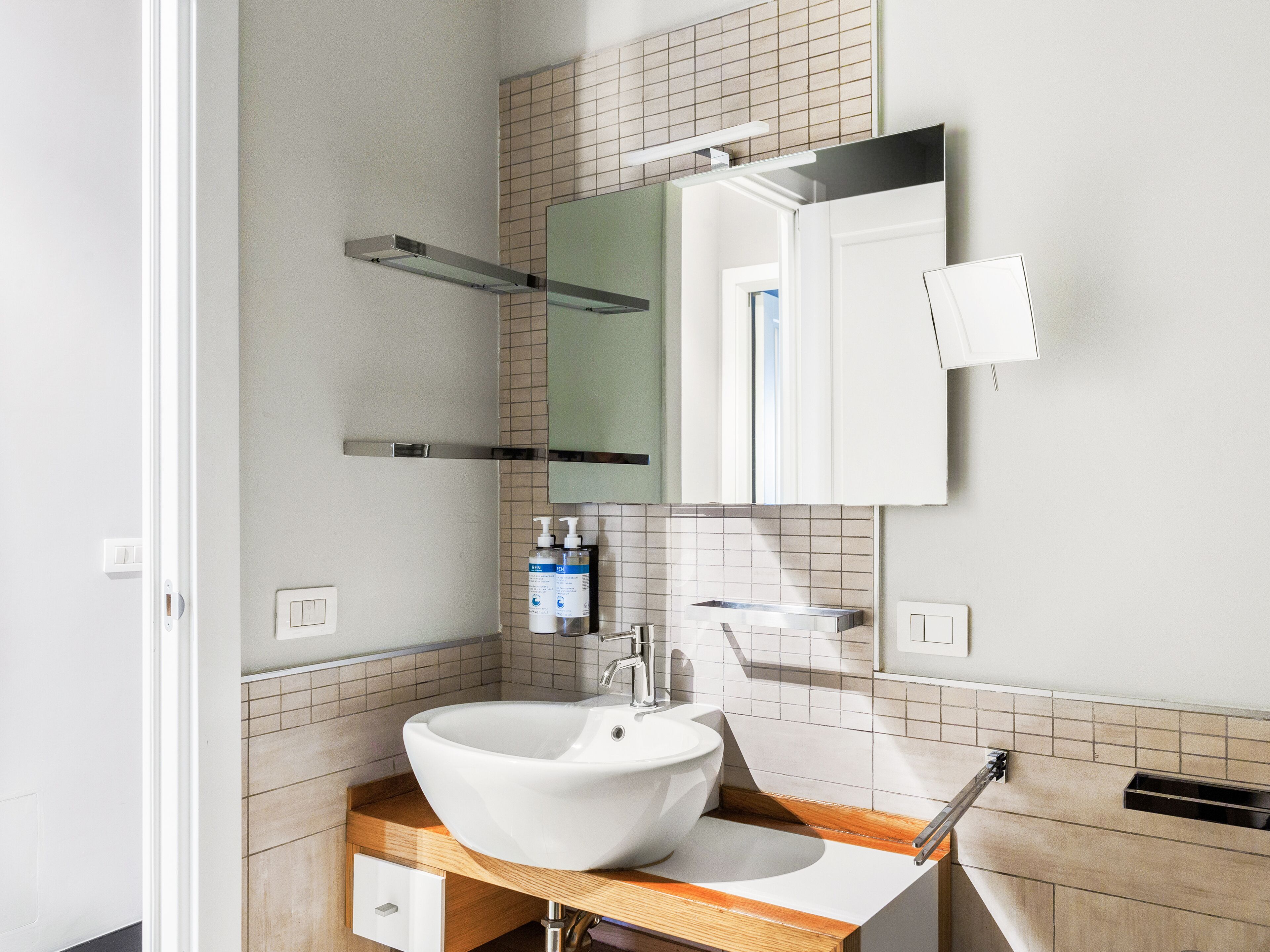 A modern bathroom with a large white vessel sink, a mirror, and a wooden vanity.