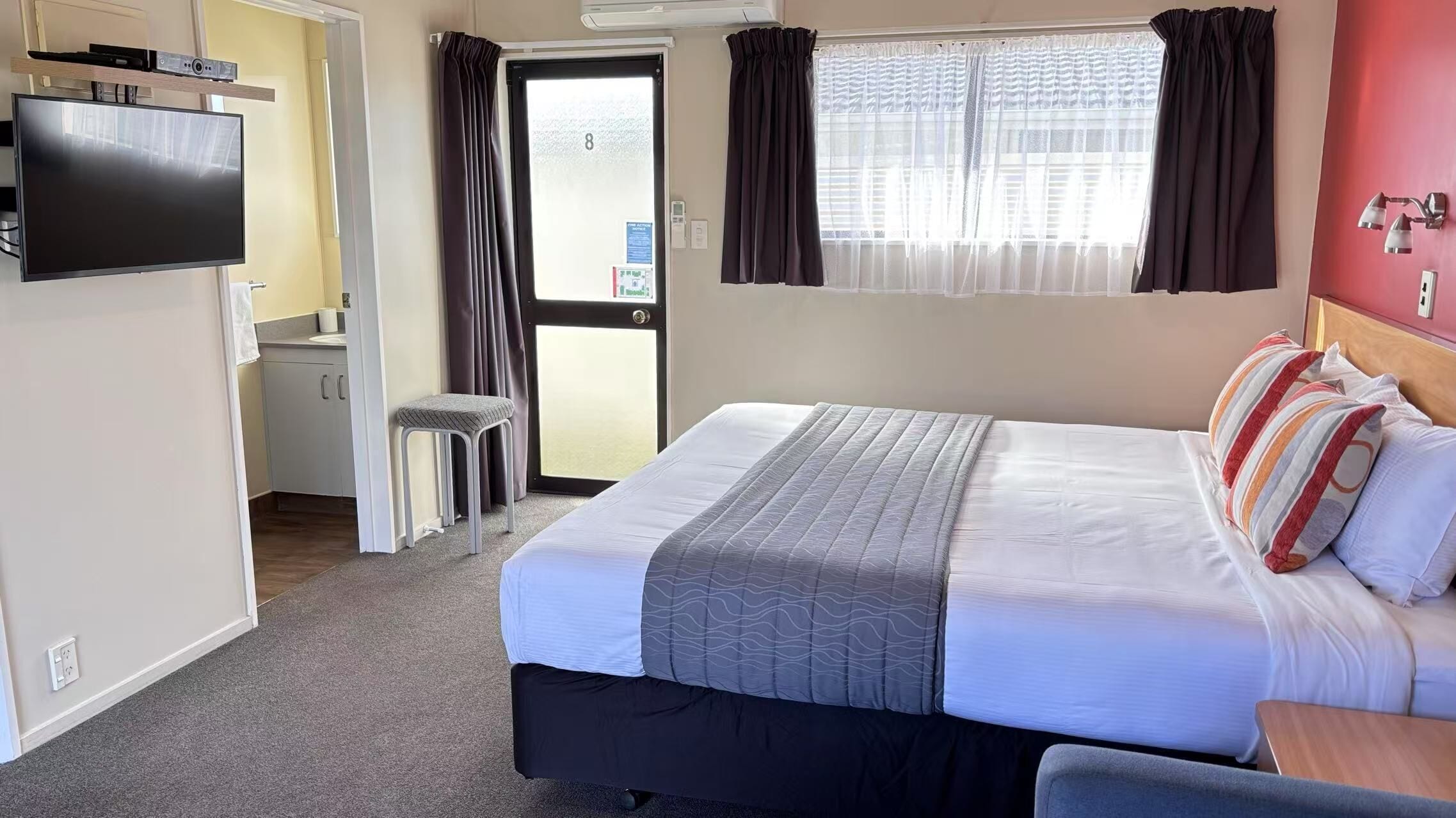 Quarto de hotel com cama, televisão, escrivaninha e janela com cortinas.