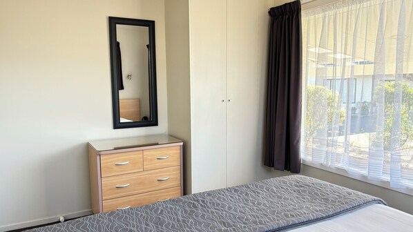 A bedroom with a bed, a dresser, a mirror, and a window with curtains.