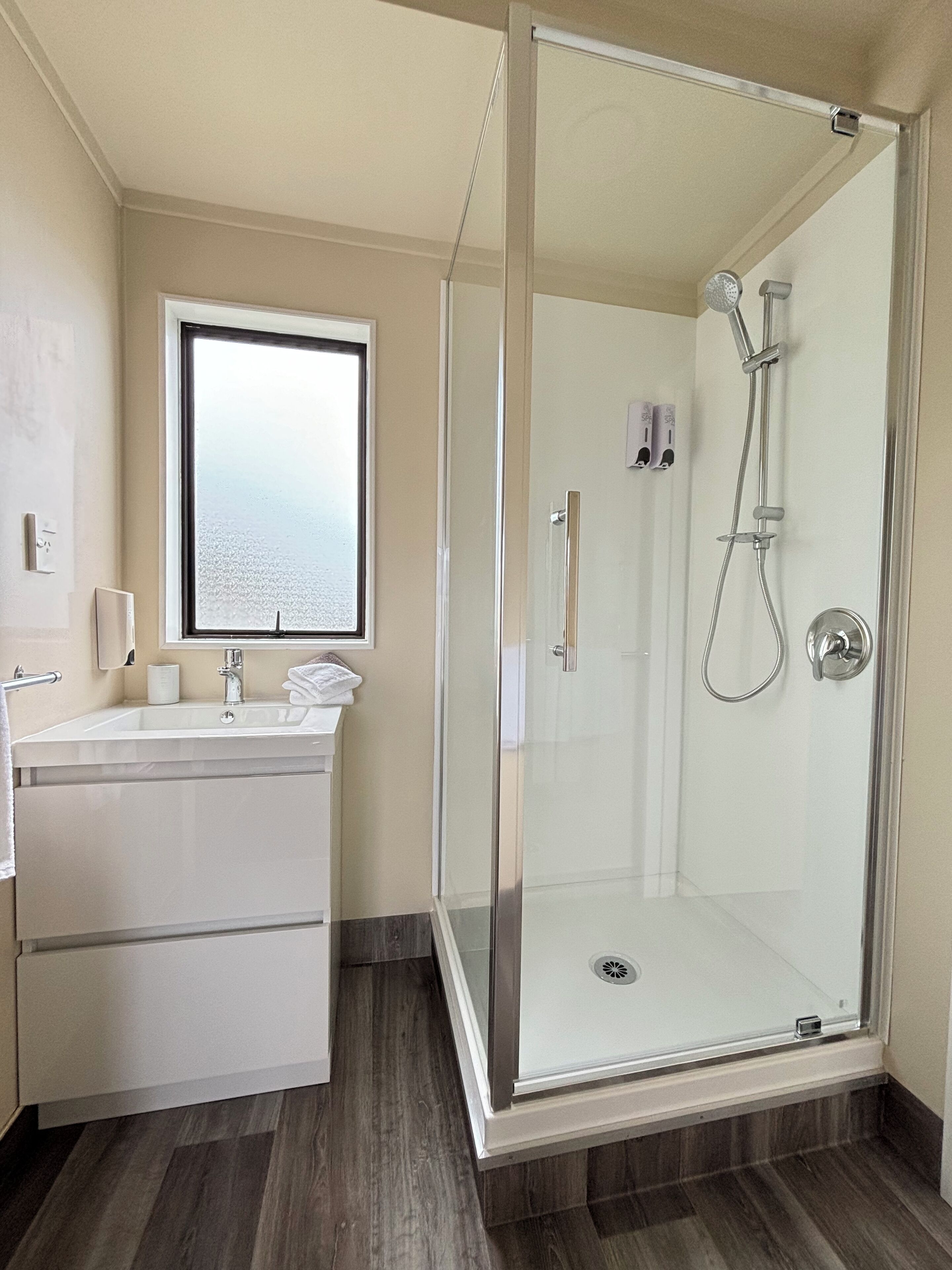A modern bathroom with a glass-enclosed shower, a vanity with a mirror, and a window.
