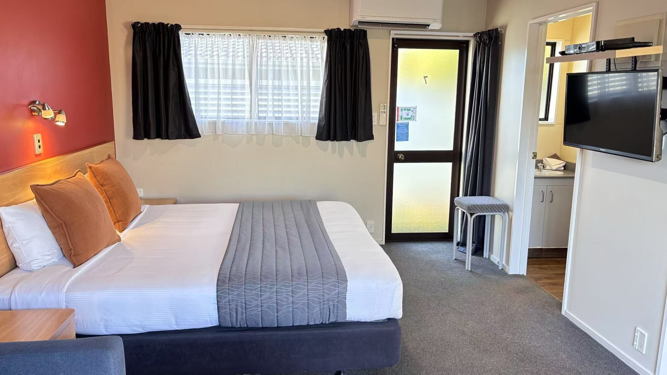 A hotel room with a bed, a TV, a small kitchenette, and a door leading to a balcony.