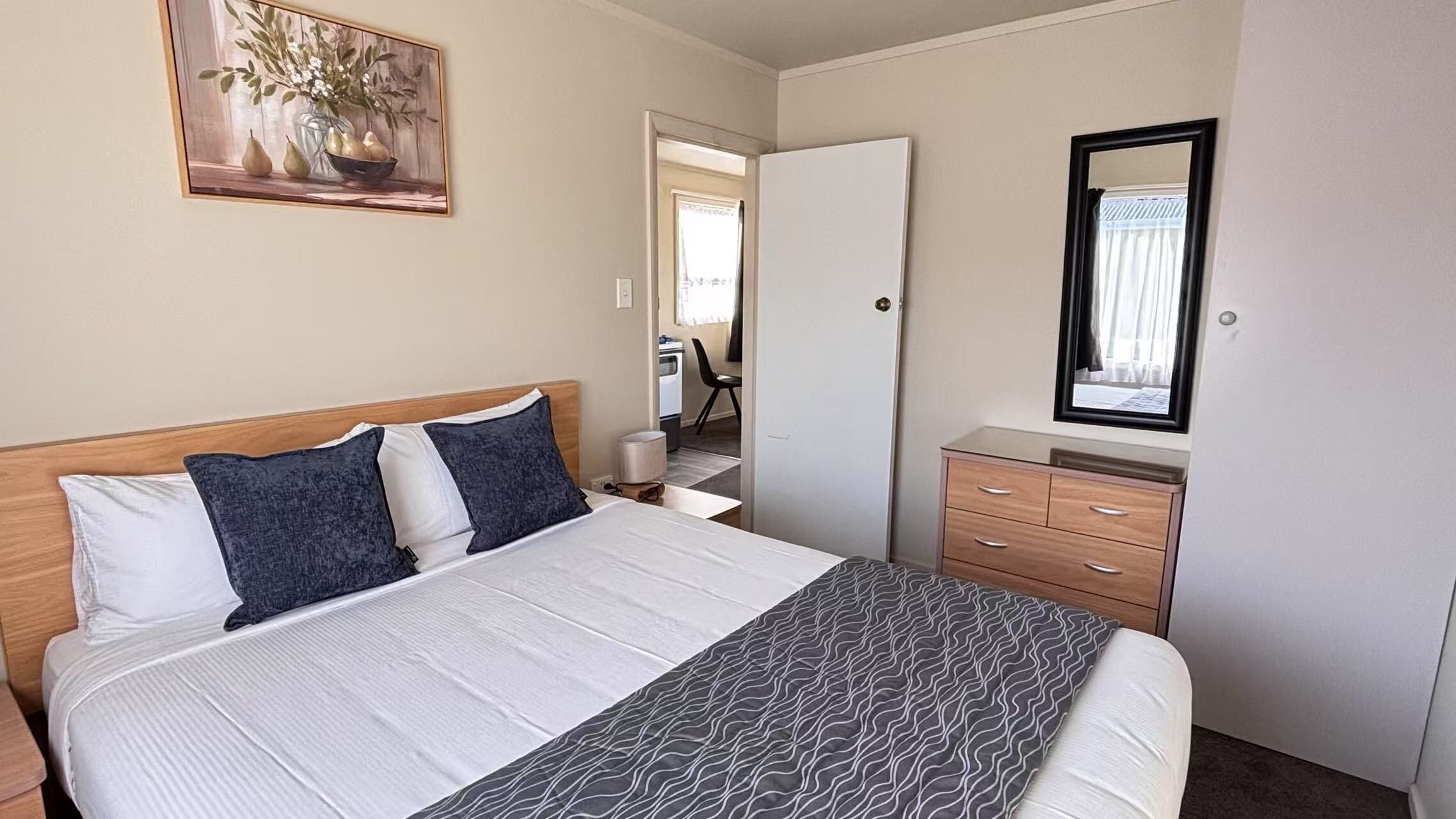 A neatly arranged bedroom with a bed, bedside tables, a dresser, and a mirror.