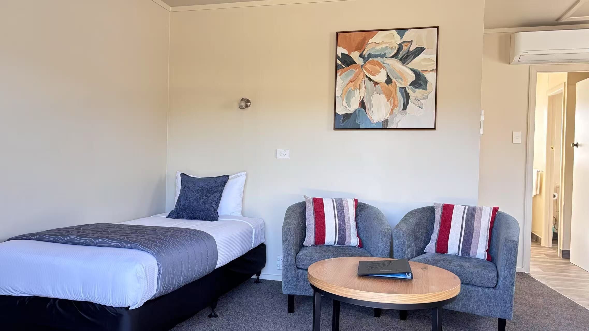 Une chambre à coucher avec un lit, deux fauteuils, une petite table ronde et un tableau accroché au mur.