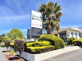 Exterior del motel Arcadia, con un gran cartel que enumera los servicios, arquitectura moderna y jardines bien cuidados.