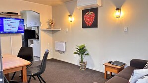 En moderne stue med sofa, spisebord med stole, fjernsyn, radiator og vægmonteret varmeovn.