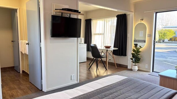 Et hotelværelse med seng, fjernsyn ophængt på væggen, spiseplads med bord og stole samt udsigt ud