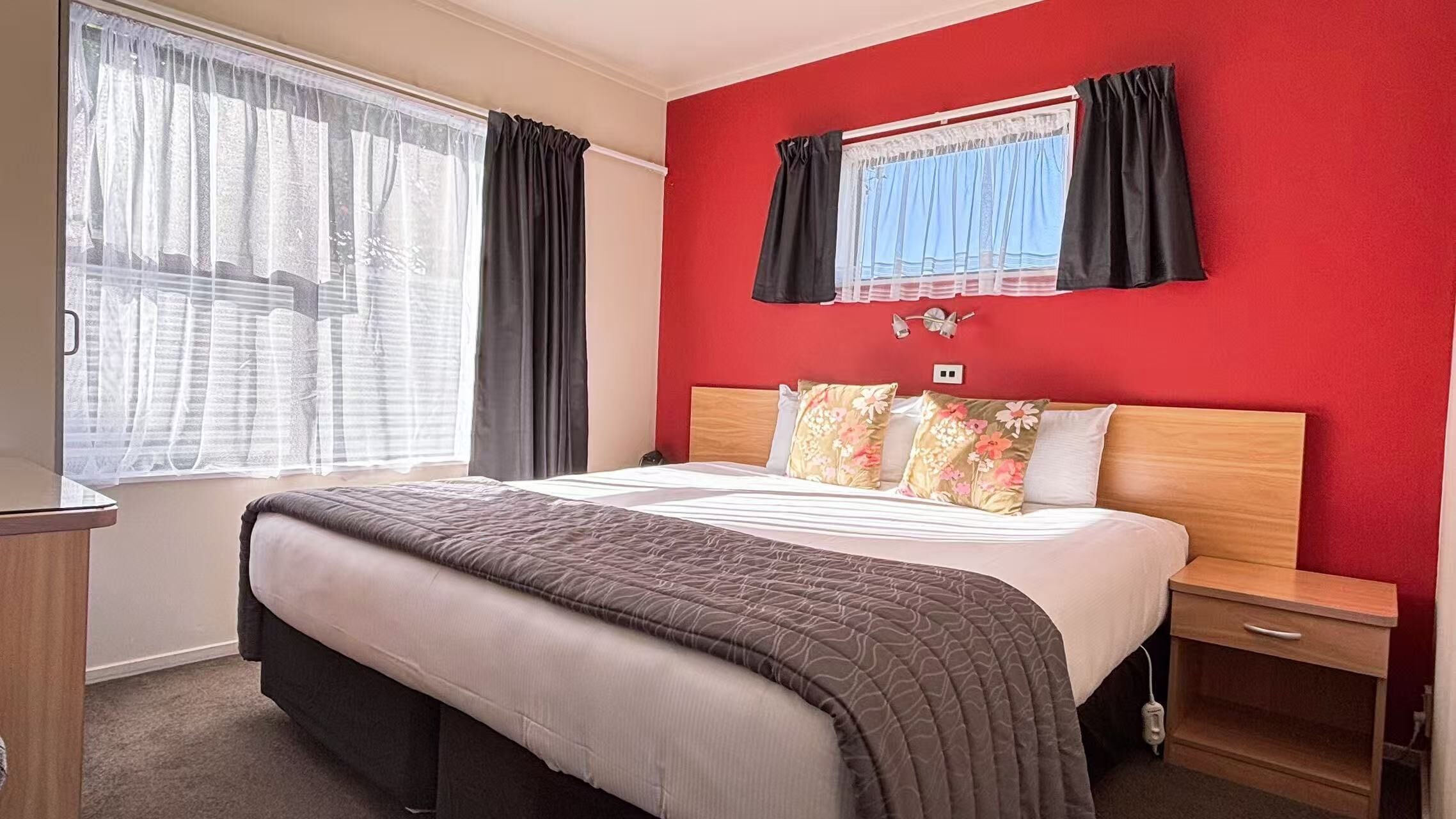 Une chambre d’hôtel avec un grand lit, une table de chevet en bois, une lampe de chevet et une fenêtre avec des rideaux.