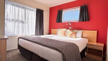Une chambre d’hôtel avec un grand lit, une table de chevet en bois, une lampe de chevet et une fenêtre avec des rideaux.