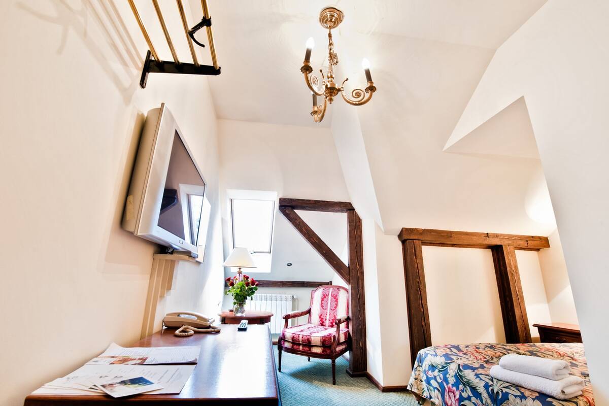 Un dormitorio con cama, escritorio, silla, candelabro y ventana.