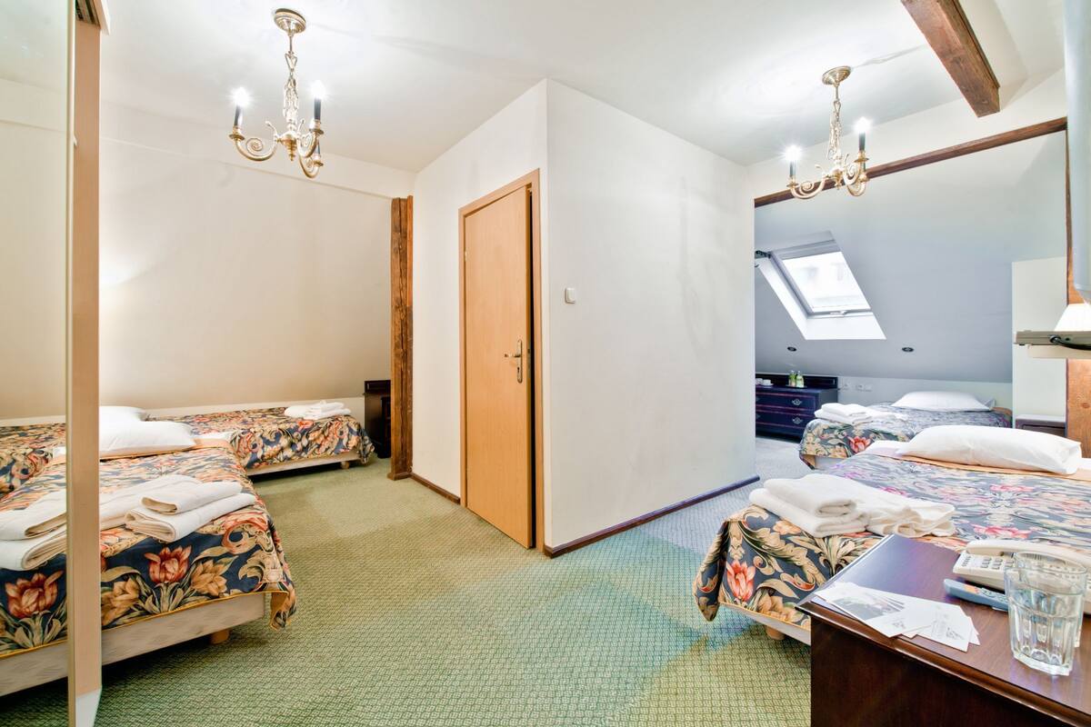 Una habitación de hotel con dos camas, una puerta de madera, un tragaluz y una araña.