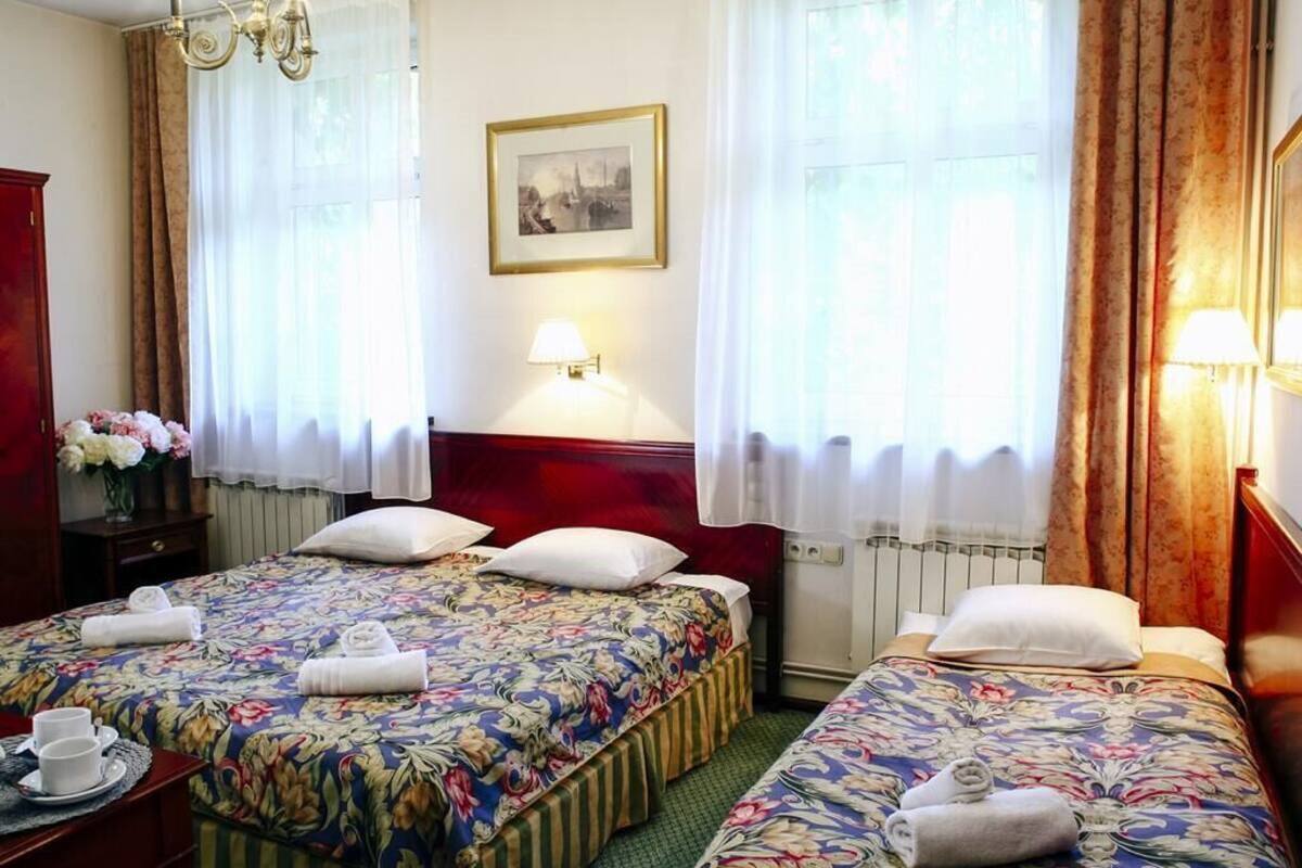 Habitación de hotel con dos camas, un candelabro, un cuadro en la pared y un florero con flores en una mesita de noche.