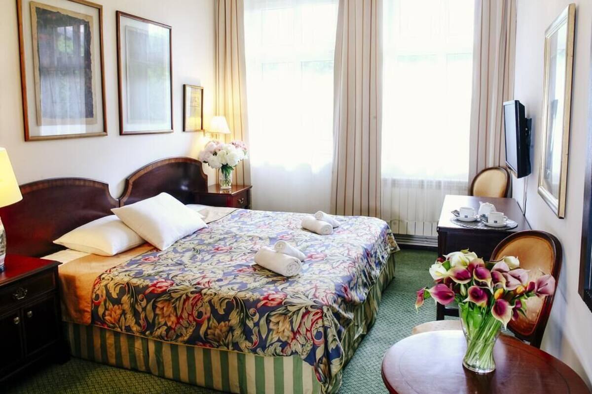 Una habitación de hotel con cama, escritorio, silla, lámpara y un jarrón con flores.