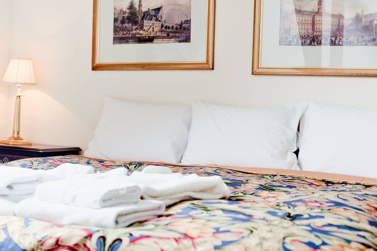 Una cama bien hecha con sábanas blancas, una colcha estampada y dos cuadros en la pared.