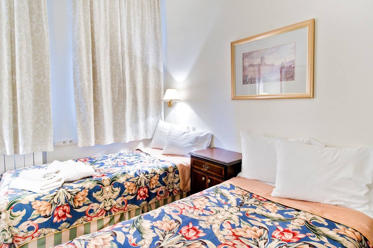 Habitación de hotel con dos camas, una mesita de noche, una lámpara y un cuadro en la pared.