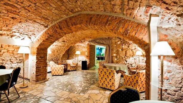 An interior with stone arches, tables, chairs, and lamps. - Aparthotel Miodosytnia (Kraków)