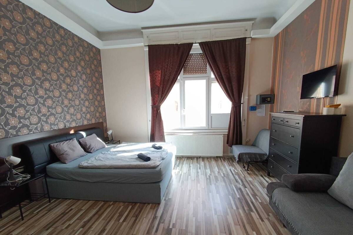 Un dormitorio con cama, cómoda, televisor y ventana con cortinas.