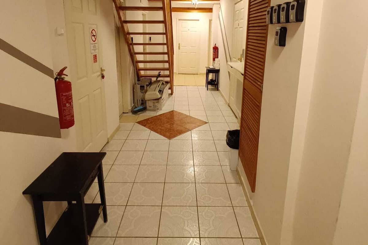 Un estrecho pasillo con una escalera de madera, un extintor, un banco y un buzón en la pared.