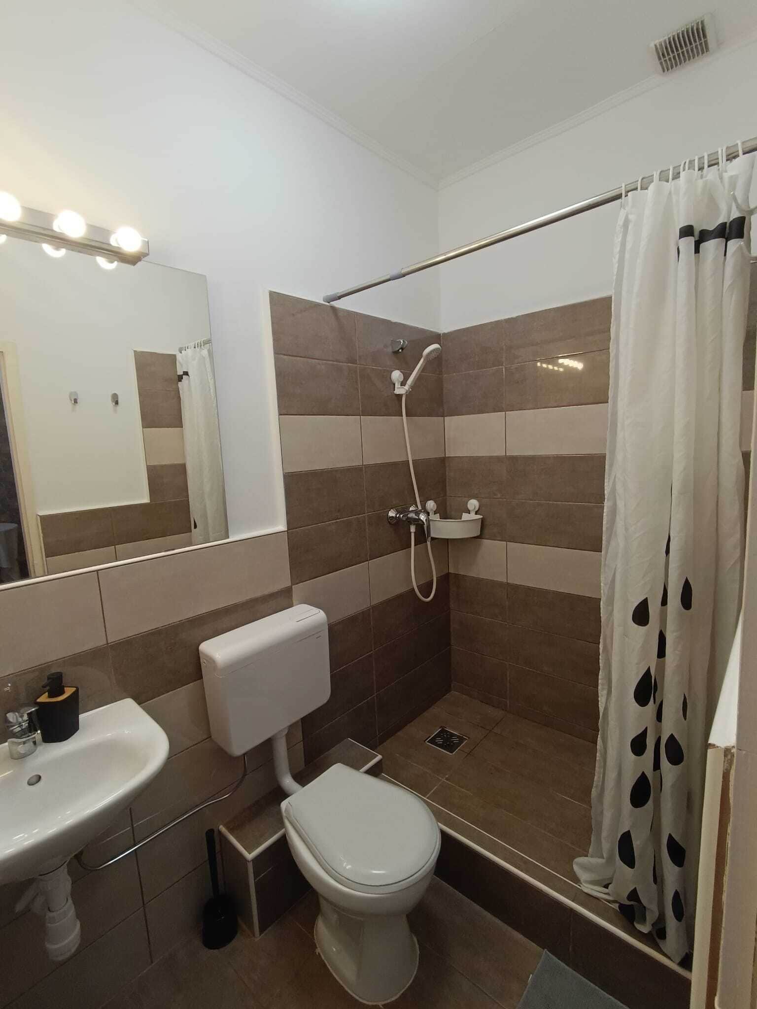 Een badkamer met douche, toilet, wastafel en een spiegel met verlichting.