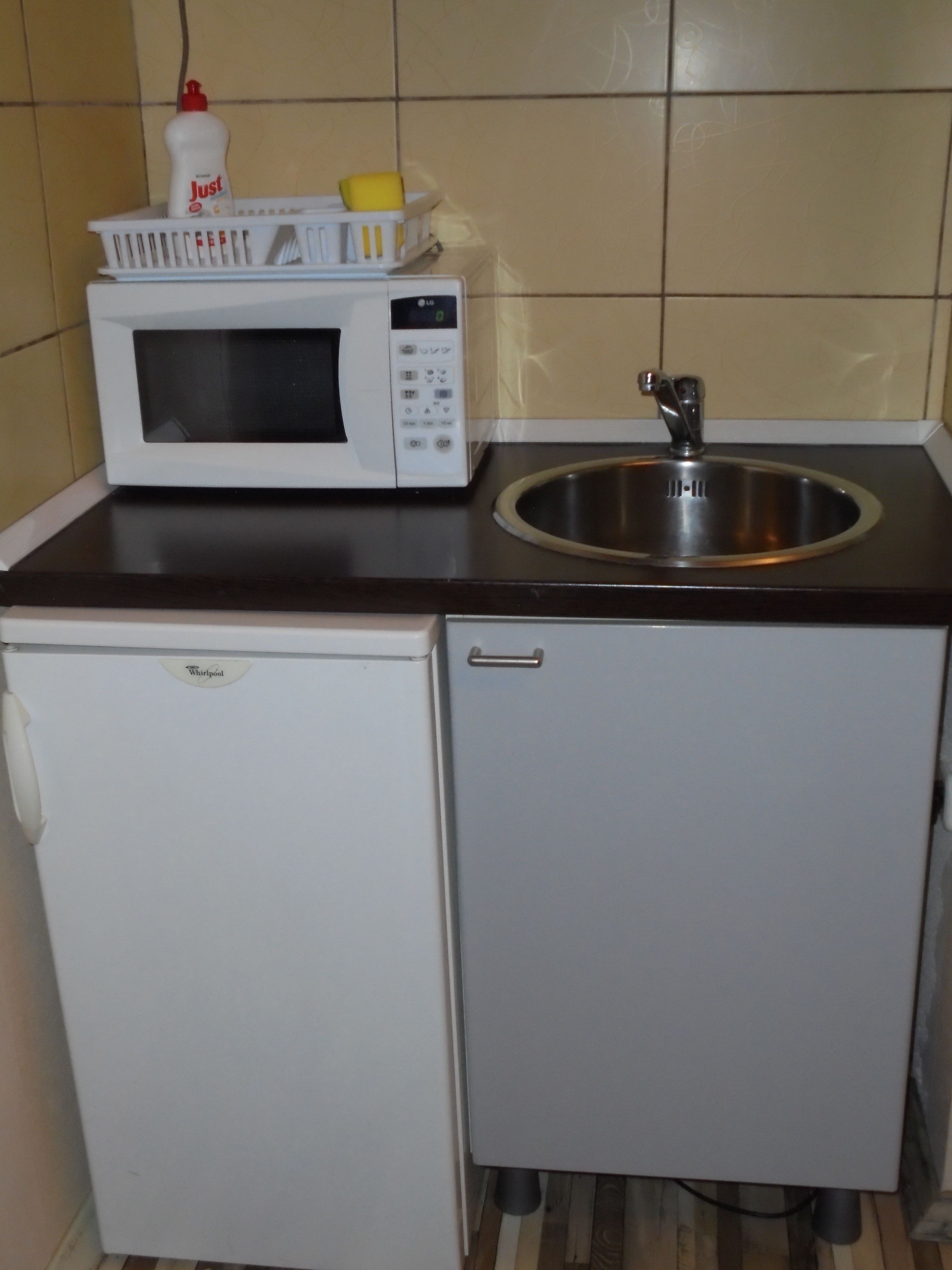 Een kleine keuken met een magnetron, spoelbak en een koelkastje.