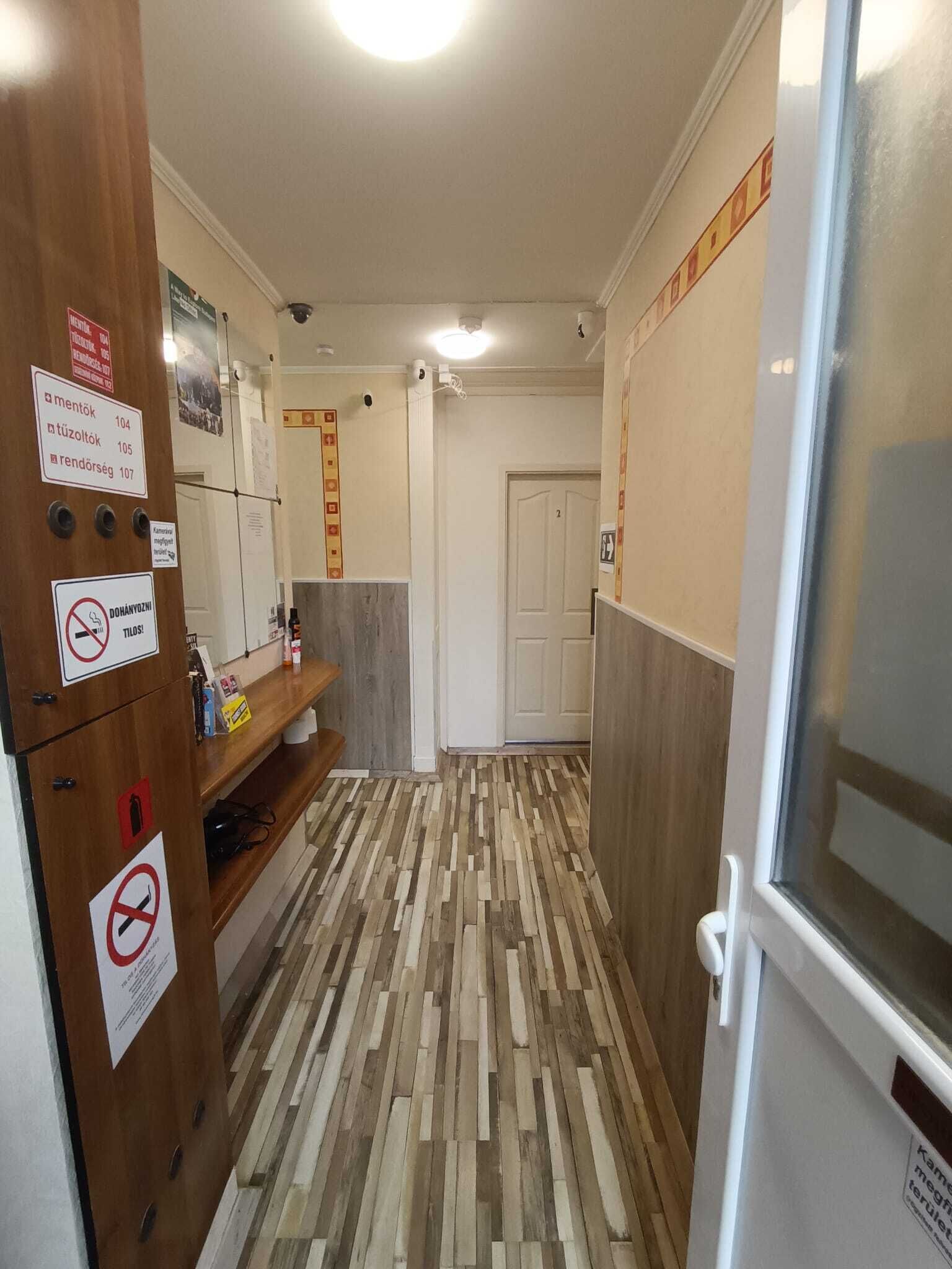 A narrow hallway with a wooden cabinet on the left, a refrigerator on the right, and a door at the end.