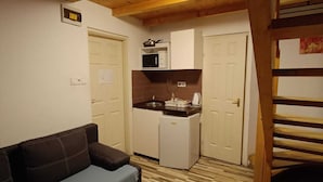 A compact living space with a sofa, kitchenette, and wooden ceiling beams.