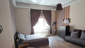A hotel room with a bed, a sofa, a small table with a chair, a TV, and a lamp.