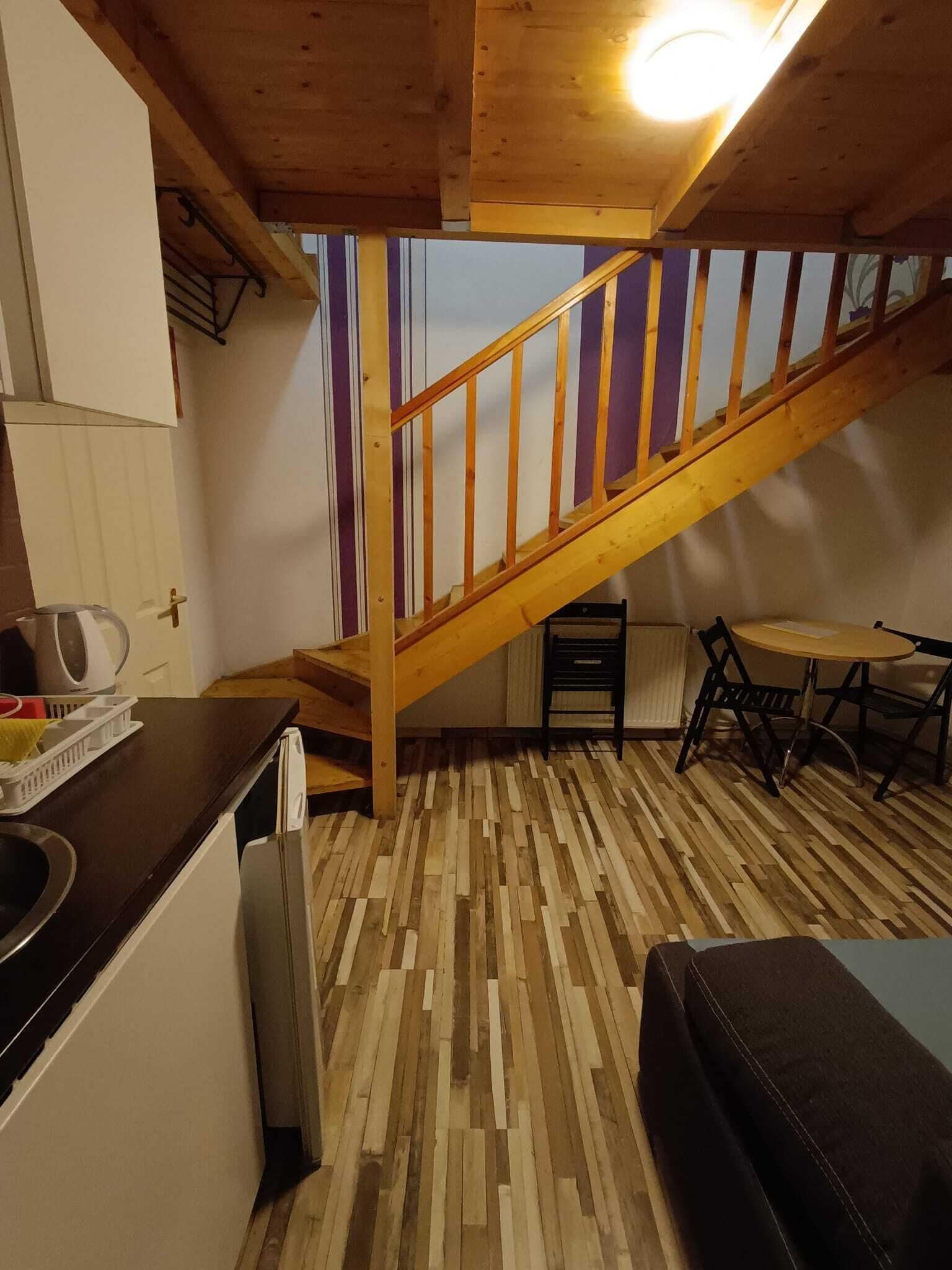 A compact kitchen with a wooden staircase, a dining area with a table and chairs, and a patterned floor.