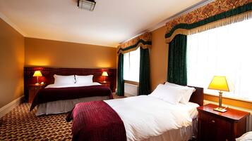 A hotel room with two beds, a wooden headboard, a patterned carpet, and a window with curtains.