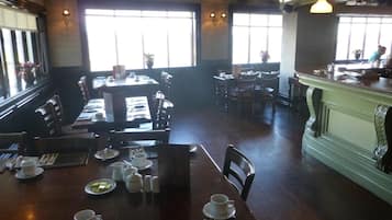 Un restaurante con varias mesas y sillas, ventanas amplias y una zona de bar.