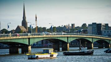 A bridge over water with boats, a church spire, and buildings in the background.