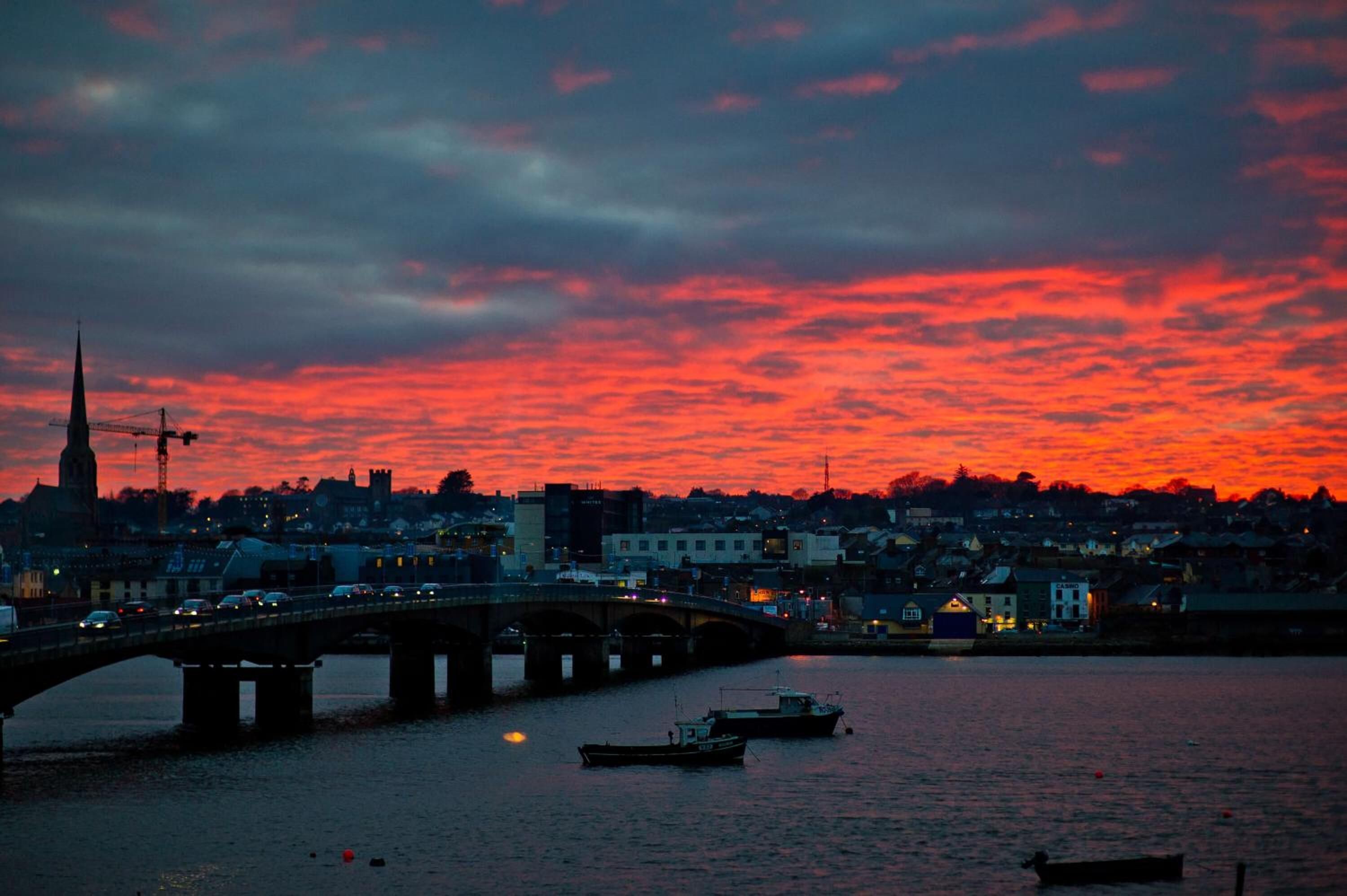 A sunset over a city with a bridge, boats, and buildings.